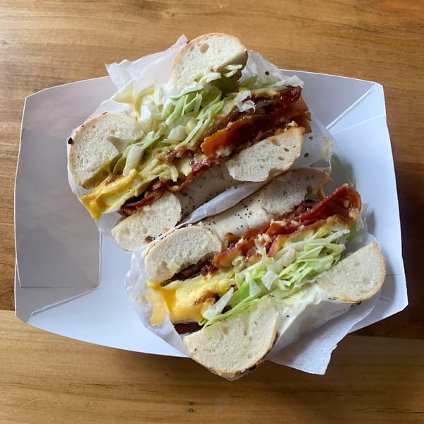 A BGL bagel sandwich, cut in half, with bacon, egg, cheese, and shredded lettuce.