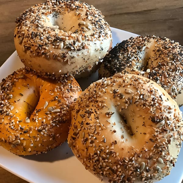 A white plate holds four BGL bagels, two everything, one poppy seed, and one sesame seed.