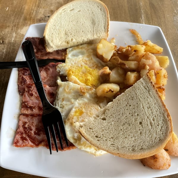 A breakfast plate with fried eggs, sliced meat, home fries, and two slices of bread.