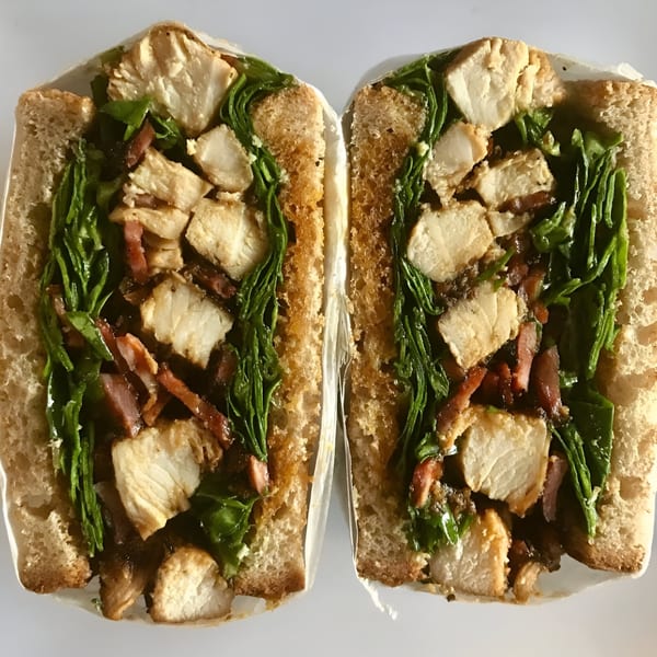 Two halves of a chicken, bacon, and spinach sandwich on toasted bread, viewed from above.