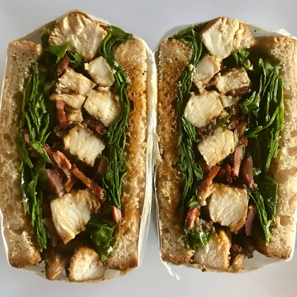 Two halves of a chicken, bacon, and spinach sandwich on toasted bread, viewed from above.