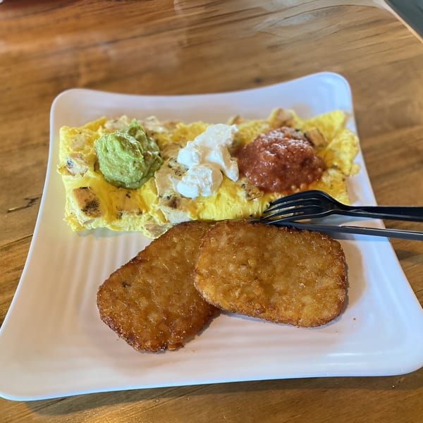 BGL's breakfast plate with an omelet topped with guacamole, sour cream, and salsa, alongside two hash browns.