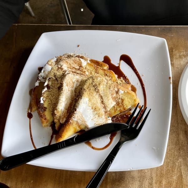 S'mores French toast with whipped cream, graham cracker crumbs, and chocolate drizzle on a white plate.