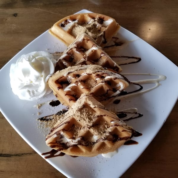 Four waffle triangles with chocolate drizzle, powdered sugar, and whipped cream on a white plate.